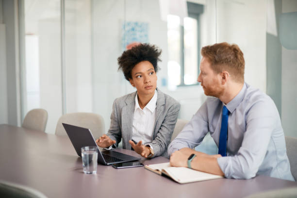 istock Black female CEO using laptop while talking to colleague in the office. 1415806704
