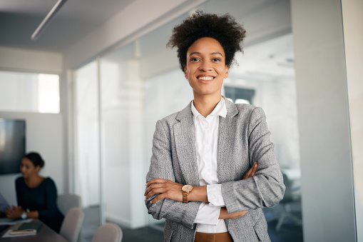 Professional, corporate businesswoman with arms crossed, in position of leadership, in marketing strategy presentation. Smiling employee standing in company boardroom for advertising business meeting