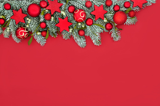 Happy holidays Christmas decorative red background border with snow fir, mistletoe and bauble tree decorations. Vivid traditional festive design for Xmas holiday season.