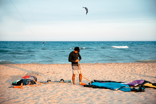 Man on a beach preparing his kite on sand beach for kitesurfing on sea waves