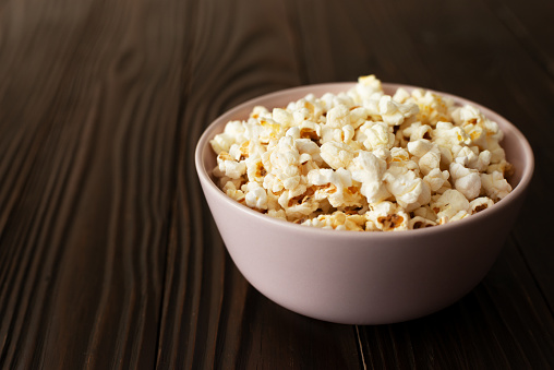 Bowl with popcorn on dark wooden table with copy-space