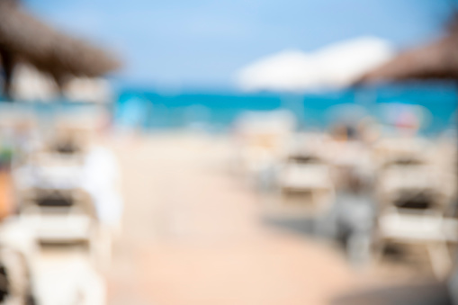 Blurred sand beach with parasol and lounge sun beds background