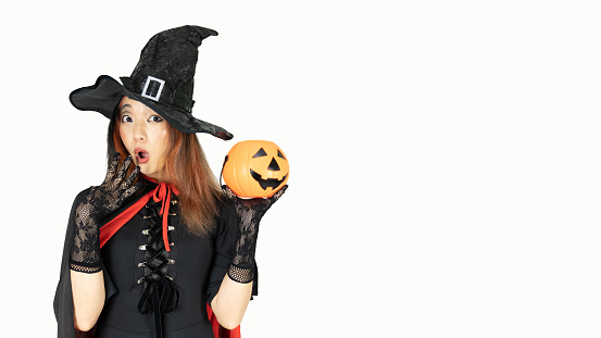 Beautiful woman with black and orange hair  in black dress and witch hat is holding pumpkin with wow emotion. Halloween concept