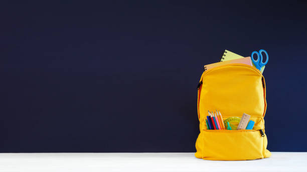 istock Backpack with different colorful stationery on table and blue background. Banner design back to school concept background. Blue chalkboard 1415816567