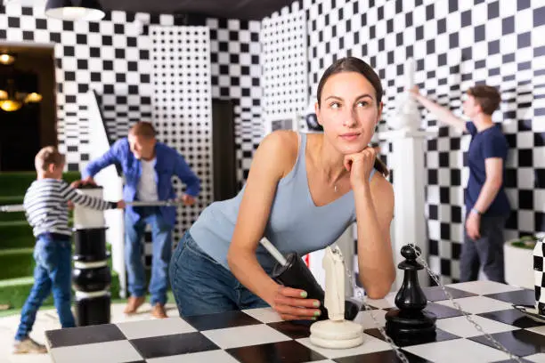 Photo of Pensive young woman standing near chessboard in quest room