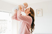 Young mother with raised arms holding baby close to face in living room