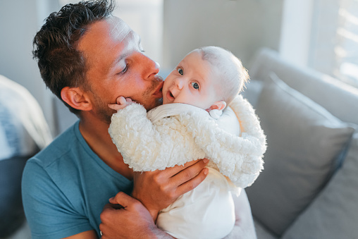 Father carrying and kissing face of baby on couch at home