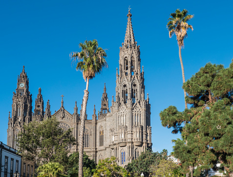 View on beautiful parish church of San Juan Bautista, impressive Neogothic Cathedral in Arucas, Gran Canaria, Spain. Blue sky and palm trees background.
