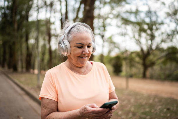 istock Senior woman using the mobile phone with headphone in a park 1415824688