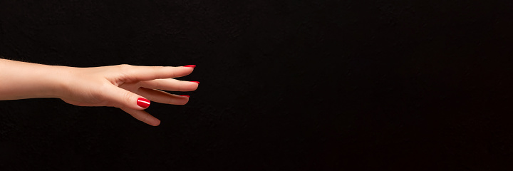 Female hand with beautiful manicure - red nails on dark black background with copy space banner. Wide panoramic header