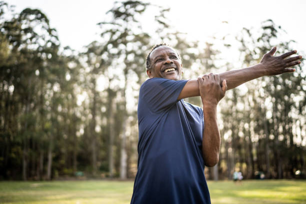 starszy mężczyzna rozciągający się w parku - breathing exercise jogging exercising relaxation exercise zdjęcia i obrazy z banku zdjęć