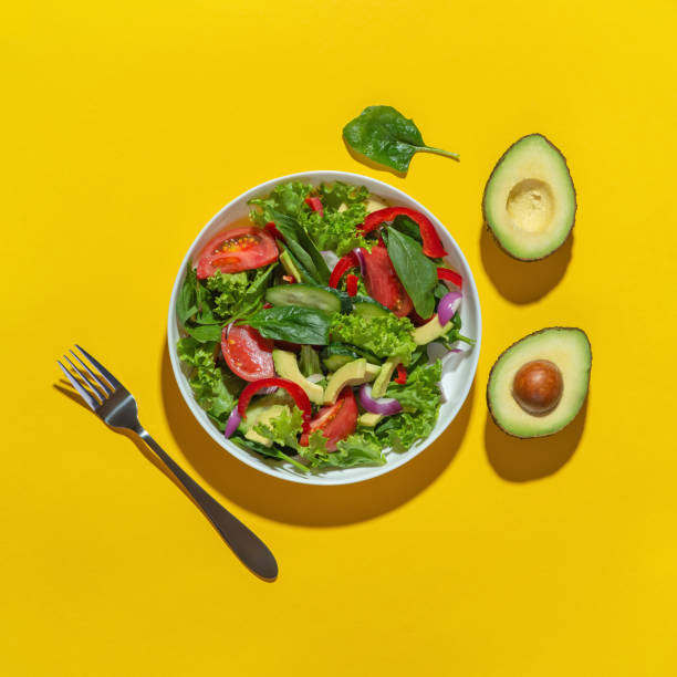 istock Vegetable salad with avocado in a white plate on a yellow background. Cooking. Diet. 1415836730