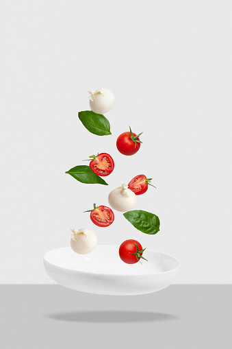 Salad with tomatoes, mozzarella and basil on a white plate. Flying ingredients, Levitation.