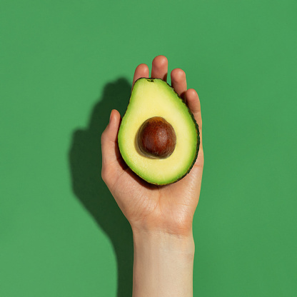 Half of a fresh ripe avocado in a female hand on a green background