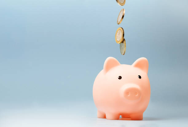 istock Pink piggy bank with falling coins on blue background 1415840367