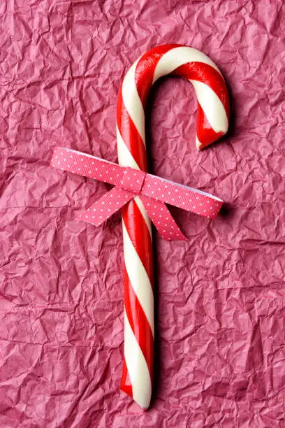 Closeup of an old fashioned candy cane with a polka dot bow. Vertical format on crumpled red tissue paper.