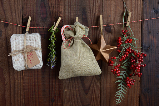 Christmas gifts and decorations hanging from twine against a dar rustic wood wall. Horizontal format.