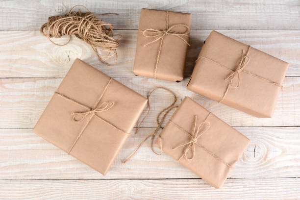 imagen de ángulo alto de cuatro paquetes marrones envueltos con papel marrón liso y atados con cordel sobre una mesa de madera rústica blanca. - 4 string fotografías e imágenes de stock