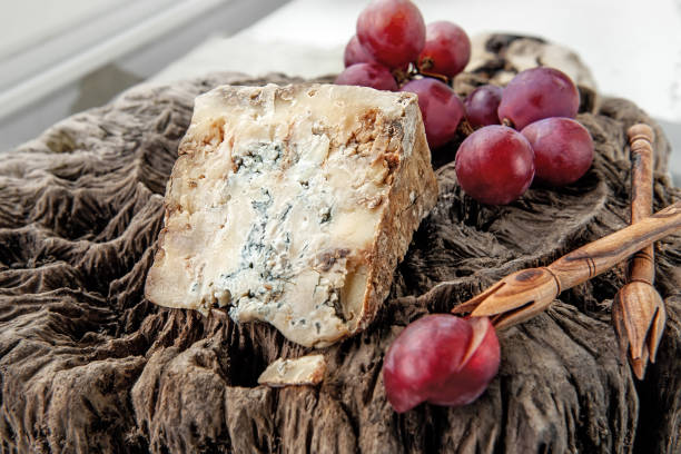 A piece of blue Stilton cheese on a wooden antique background with large red grapes. Close up stock photo