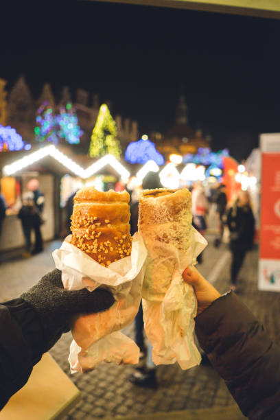 man and woman holding a sweet traditional polish roll. dessert with chocolate on background of the european city christmas market. sweet traditional street food in poland. - prague christmas bildbanksfoton och bilder