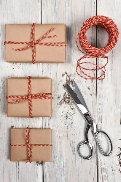 Top view of a group of plain wrapped Christmas presents on a rustic wood surface with scissors and twine.
