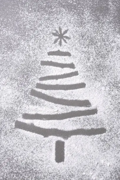 Christmas tree shape in flour sprinkled on a baking sheet. The tree shape is formed my a void in the flour.