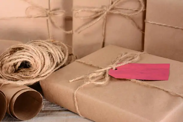Closeup of a group of Christmas packages wrapped with plain brown paper and twine. Horizontal format on a wood table.