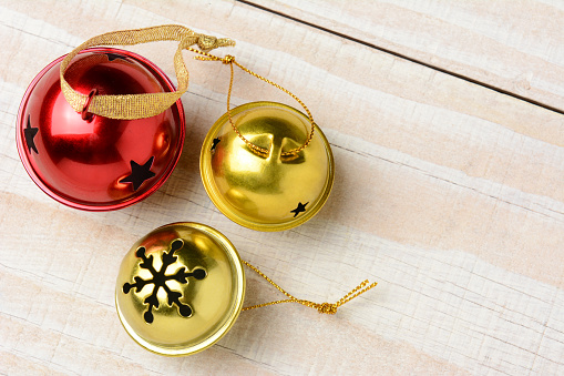 High angle closeup of three jingle bells on a white wood table. Two gold bells and one red in horizontal format with copy space.