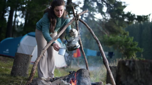 Woman pouring hot tea from campfire in the morning on a wild camping.