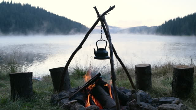 Morning on wild camp with hot tea in vintage kettle over campfire.