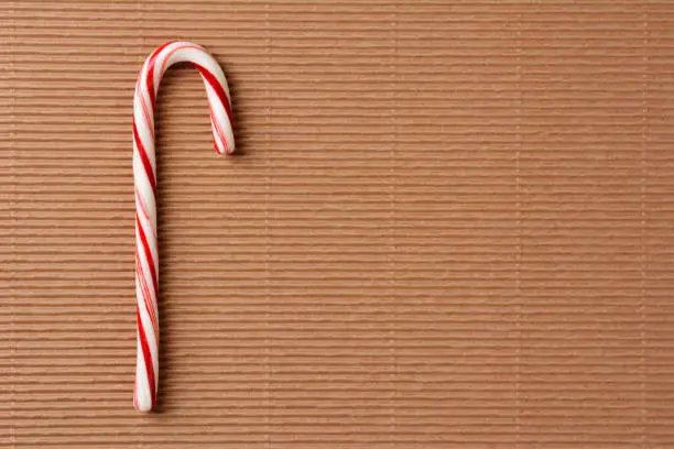 Overhead closeup view of a single candy cane on a sheet of corrugated cardboard. Horizontal format with copy space.