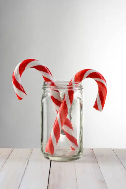Two Candy Canes in a mason jar. The jar is on a rustic white wood table with a light to dark gray background.