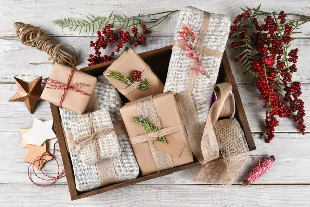High angle view of a wood box filled with Christmas presents surrounded by wrapping tools and supplies both natural and man made.