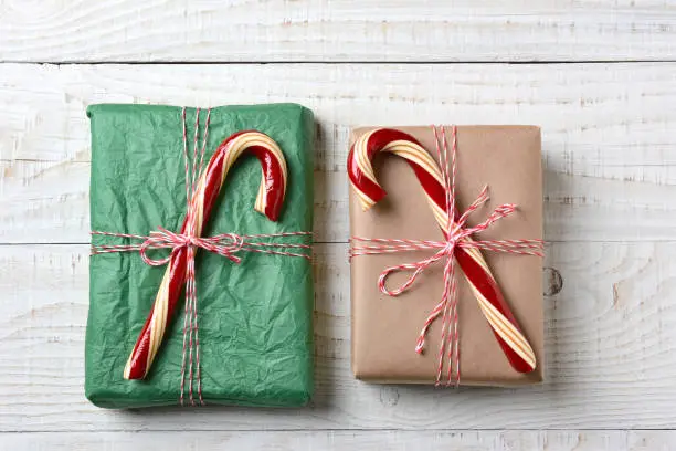 Two Wrapped Christmas presents tied with string and topped with large old fashioned candy canes, Horizontal format. Gifts are wrapped with plain paper one brown one green.