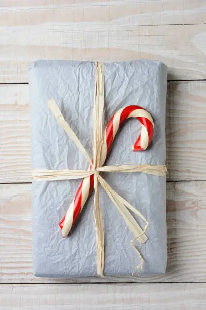 High angle shot of an old fashioned Christmas present. The gift is wrapped in crumpled tissue paper and tied with raffia. A large candy cane is on top of the present.