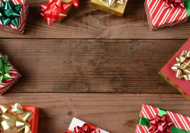 A high angle view of a group of Christmas presents on a rustic wooden floor. The presents are scattered around the edges of the frame leaving an empty middle for your object or copy.