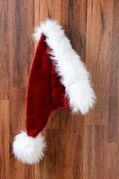 Closeup of a Santa Claus hat hanging from a nail on a rustic wooden wall.  Vertical Format.