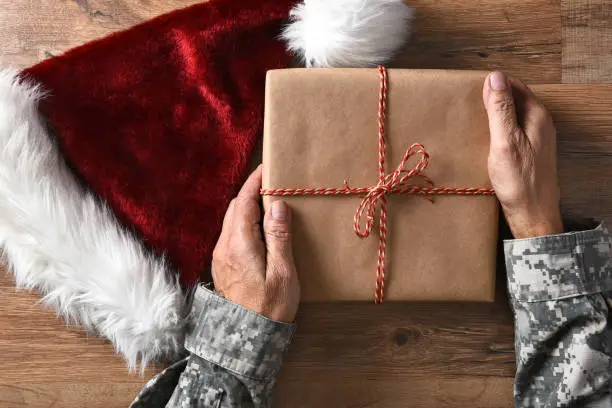 Closeup of a soldier holding a Christmas present on a wood table with a Santa hat.