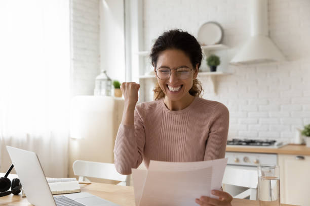 Woman sit in kitchen read paper from bank feels excited Euphoric Hispanic woman sit in kitchen read paper notification from bank about last loan payment feels happy, get job promotion letter, learn sales growth look excited. Great unbelievable news concept savings account stock pictures, royalty-free photos & images
