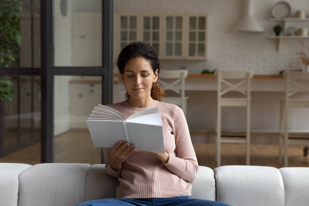 istock Focused Hispanic woman sitting on cozy sofa reading book 1415850853