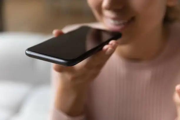 Photo of Close up female hand holds smartphone near mouth using speakerphone