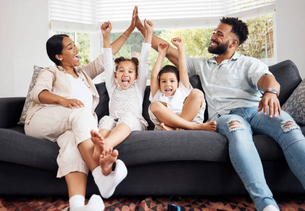 des parents heureux et des enfants excités célèbrent sur le canapé tout en regardant la télévision. temps amusant en famille, détente à la maison et liens. mère et père high five, les enfants encouragent la victoire de l’équipe sportive. - child celebration cheering victory photos et images de collection