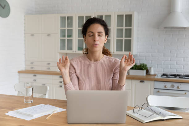 woman sit near laptop makes calming exercises to reduce stress - yoga business women indoors imagens e fotografias de stock