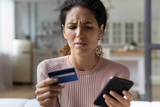 Frown woman holding card and cellphone experiences problems with e-payment