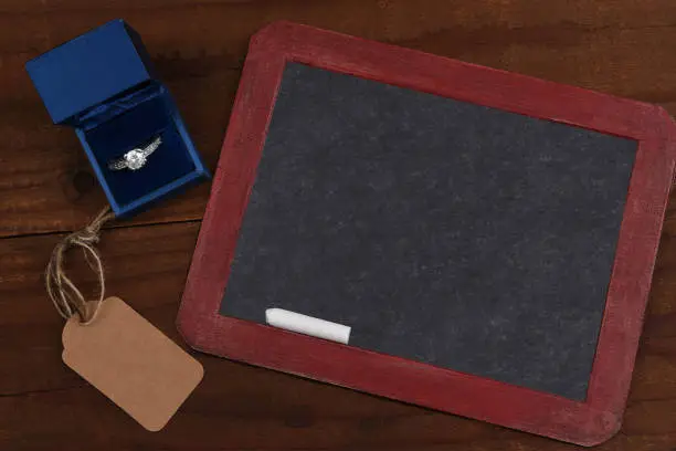 A vintage blank slate chalkboard with diamond ring and blank gift tag on a rustic wood surface.