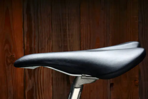 Closeup of a black biicycle saddle and seat post against a wood background.