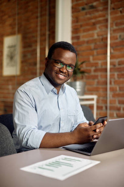 istock Happy black businessman texting on cell phone while working in the office and looking at camera. 1415855001