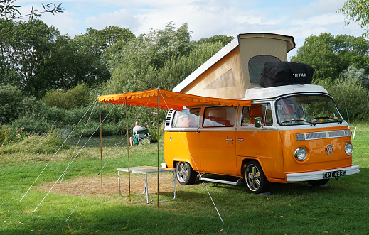 St Neots, Cambridgeshire, England -  August 13, 2021: Classic  Orange  Volkswagen  Camper Van parked on Camp Site  by river with top up and Awning