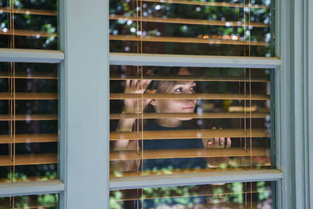 istock Young woman looks in big window with white frame through protective brown shutter enjoying view 1415864064