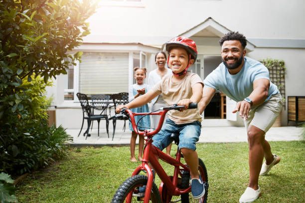 학습, 자전거 및 자랑스러운 아빠는 어린 아들에게 가족 가정 정원에서 안전을 위해 헬멧을 착용하면서 타도록 가르칩니다. 활동적인 아버지는 밖에서 자전거를 타는 동안 자녀를 돕고 지원합� - 생활 방식 이미지 뉴스 사진 이미지